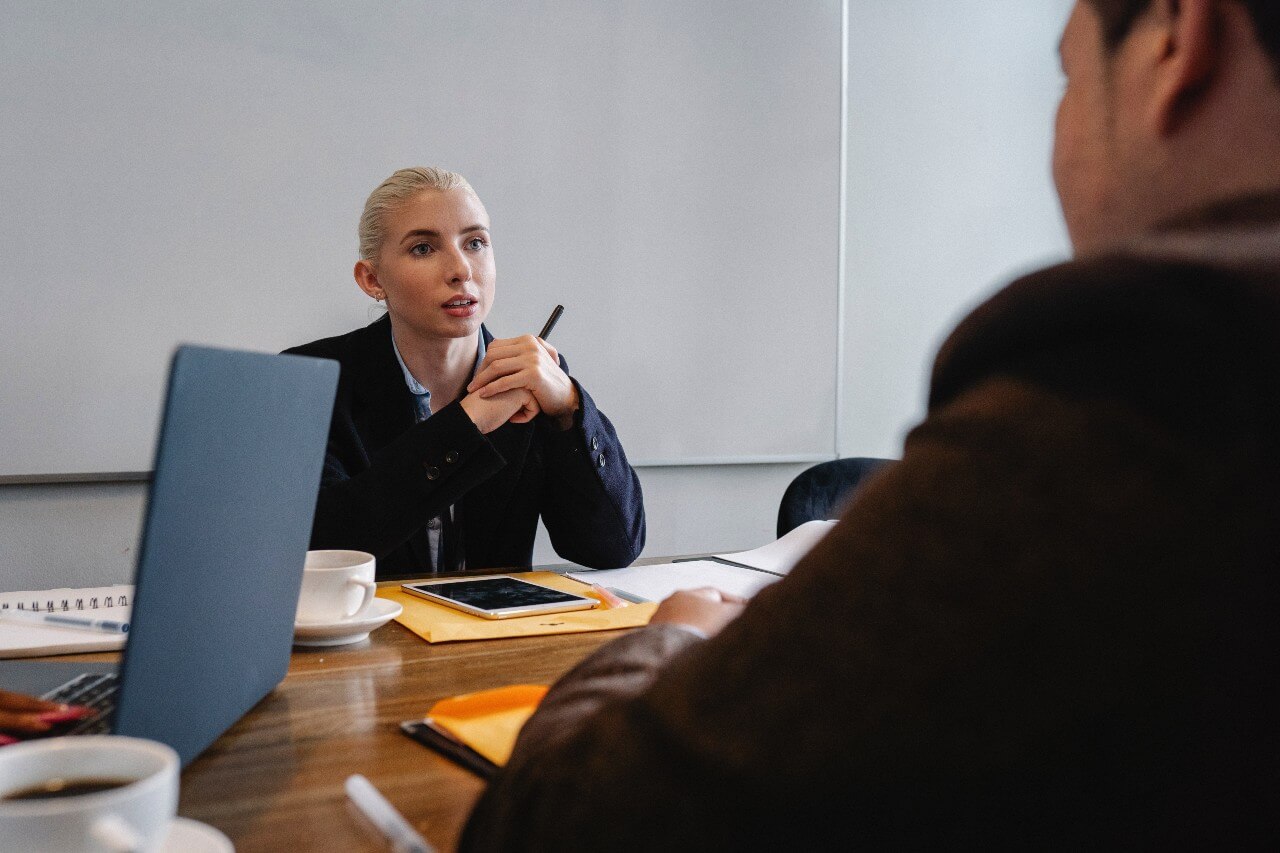 A lady in an office sits at meeting table next to laptop