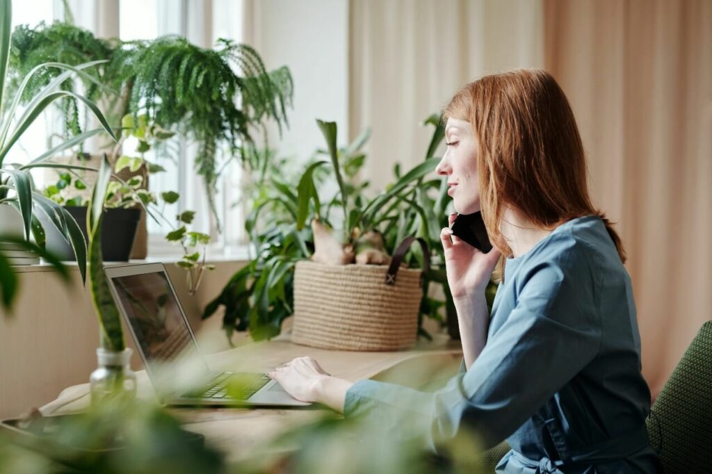 A woman sits at a desk surrounded by plants, talking on the phone