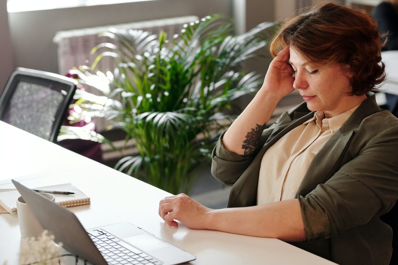 A woman sits at a desk, holding her head