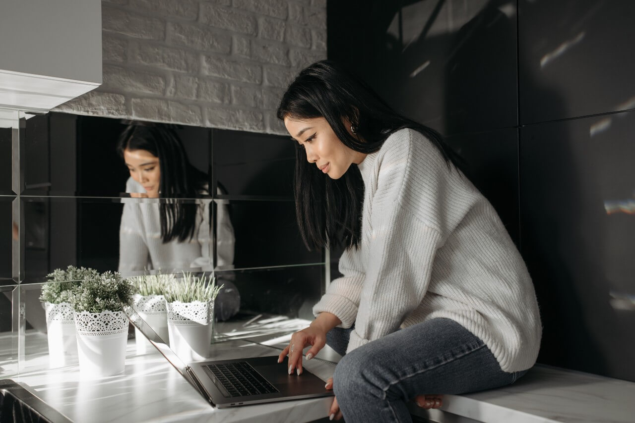 A lady with dark hair and a light coloured jumper sits at a laptop