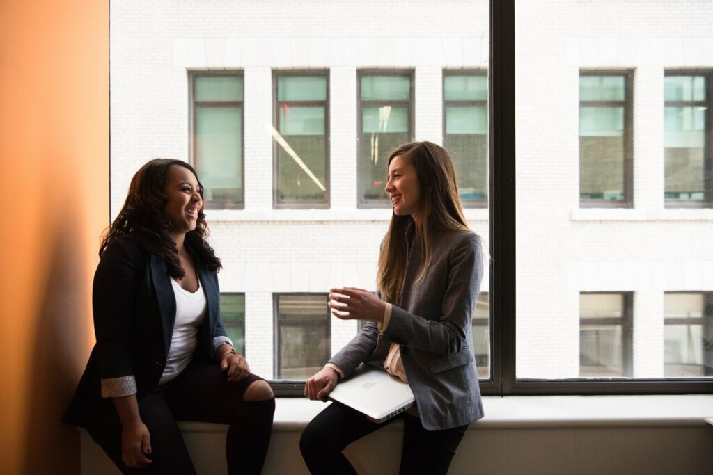 Two women sit side by side at a window, discussing work