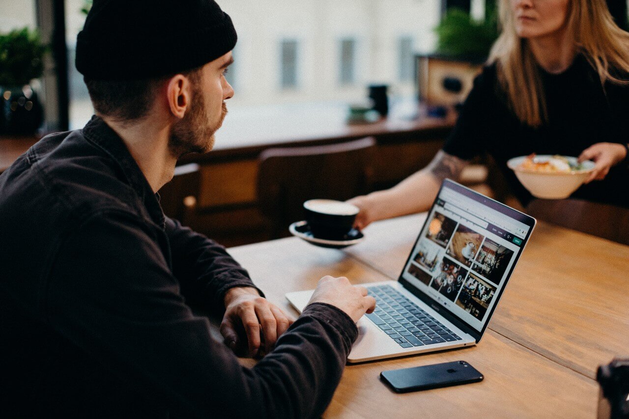 Man wearing black beanie hat sits in coffee shop working at laptop