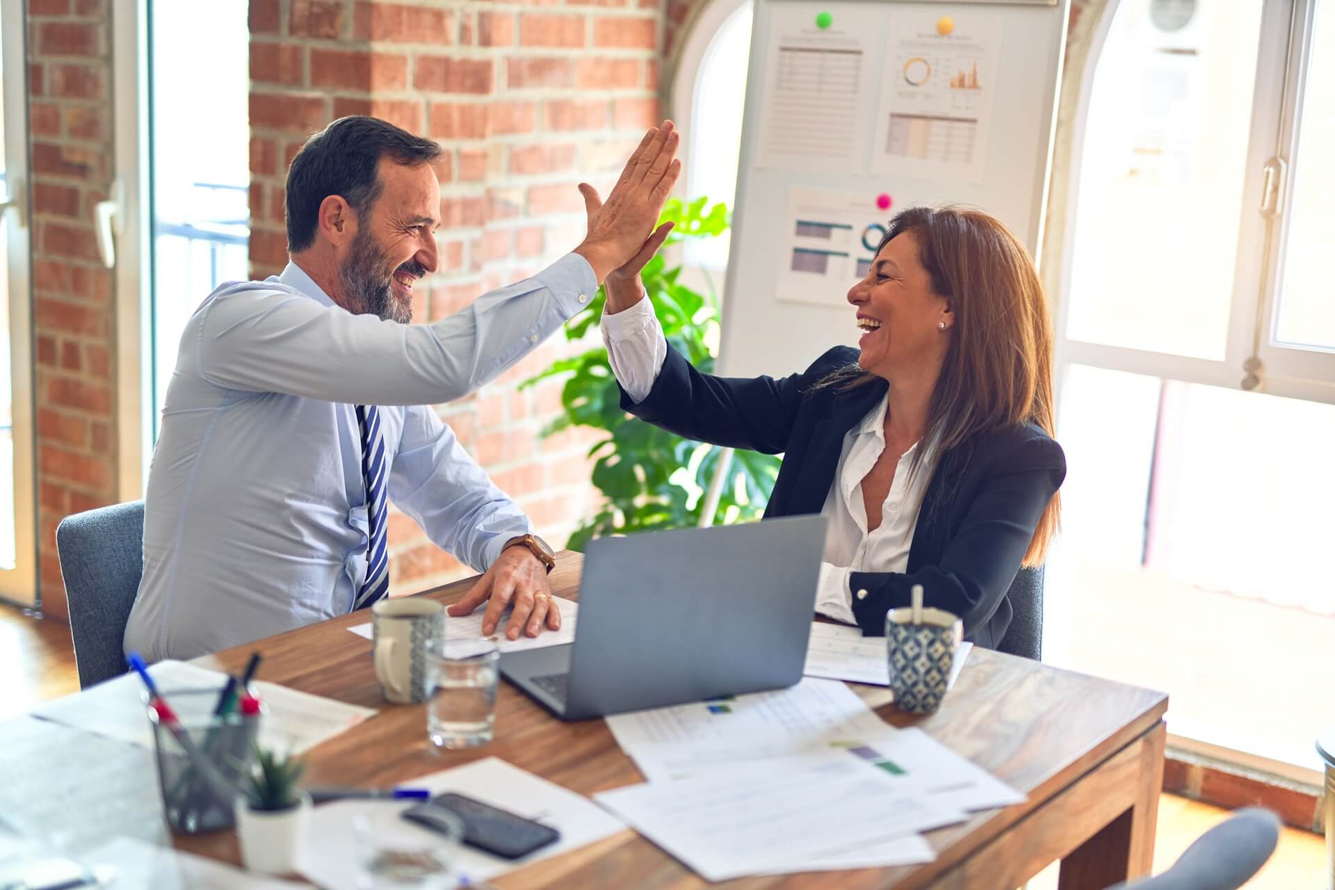 how to get a business loan with bad credit header image - image shows a man and woman sat at a desk with a laptop between them, high fiving